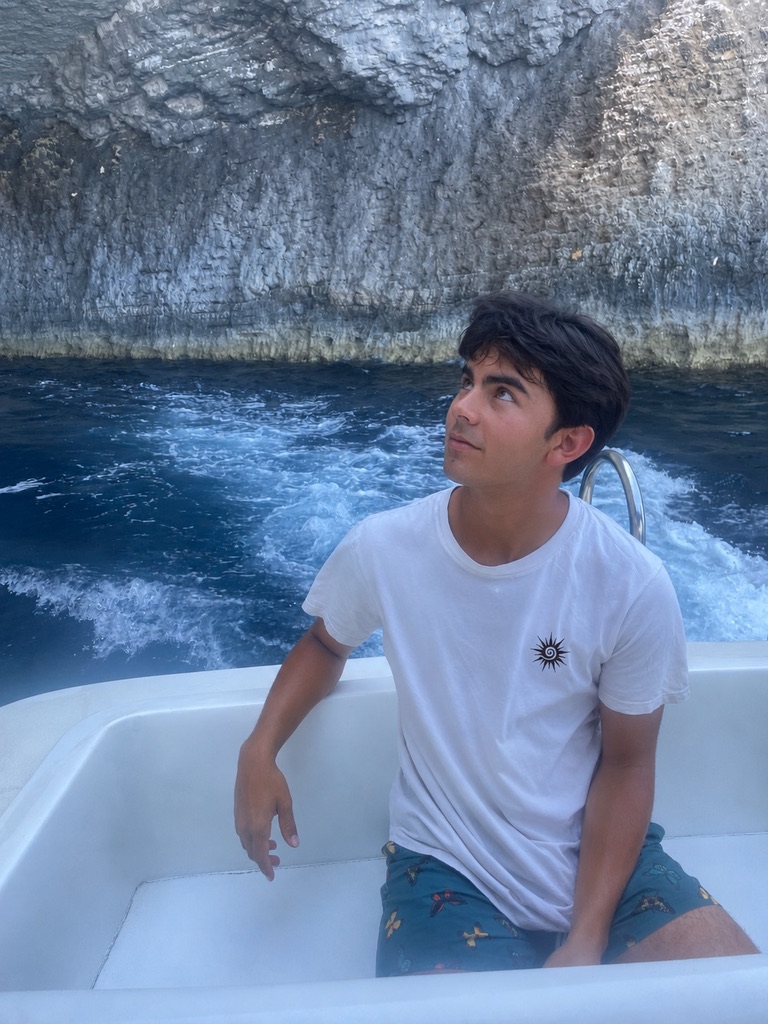 Model wearing a white Soleil sun T-shirt aboard a boat along a rocky coast